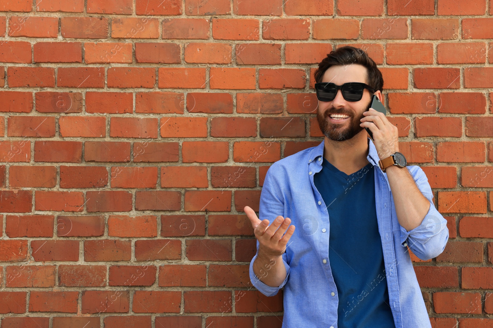 Photo of Happy man talking on phone near red brick wall. Space for text