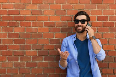 Photo of Happy man talking on phone near red brick wall. Space for text