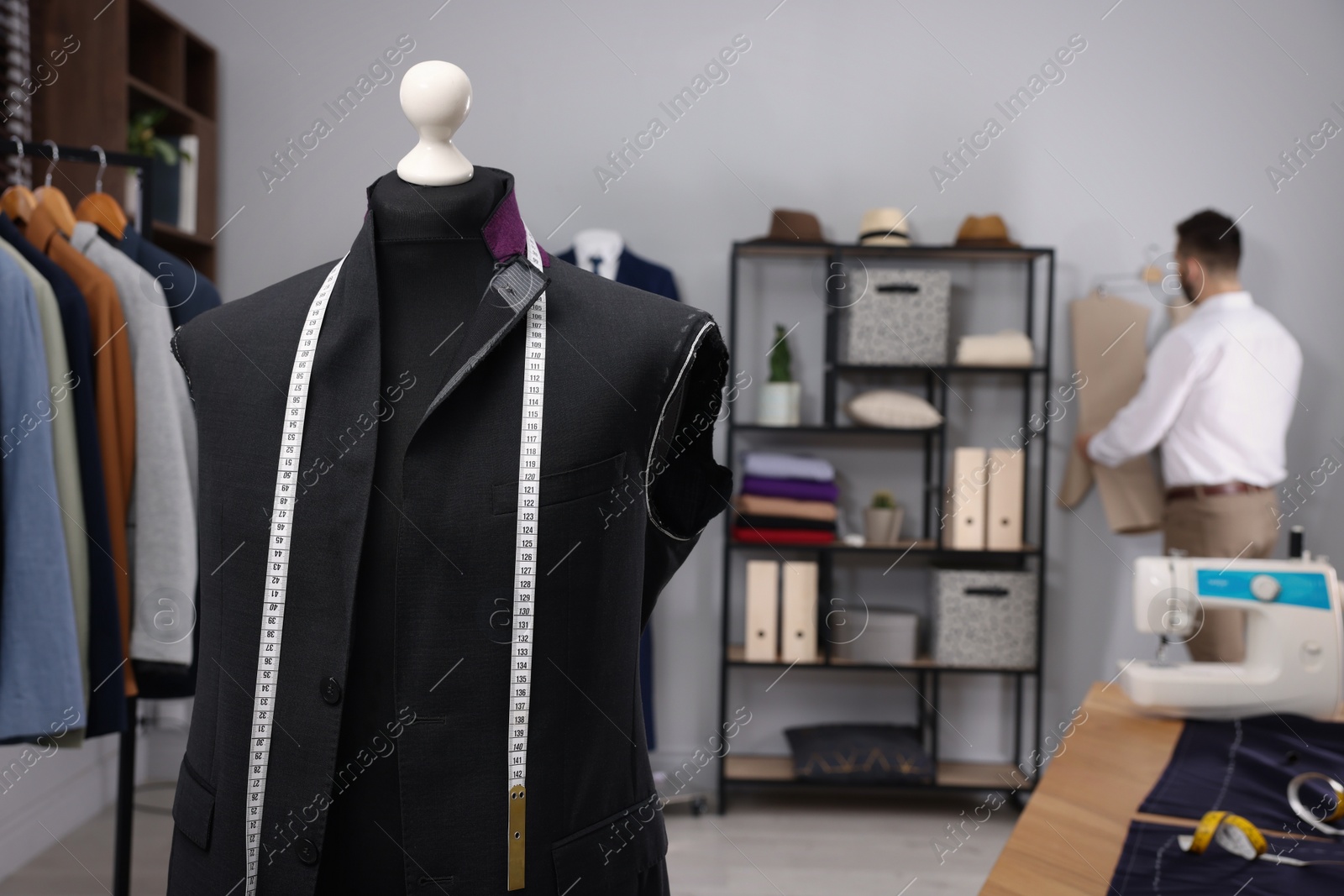 Photo of Tailor working in atelier, focus on mannequin with unfinished suit jacket and measuring tape