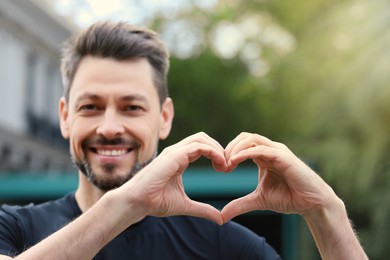 Photo of Happy man making heart with hands outdoors
