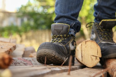 Photo of Careless worker stepping on nail in wooden plank outdoors, closeup