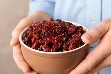 Woman holding bowl with tasty cranberries on color background, closeup. Dried fruits as healthy snack