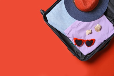 Suitcase with beach accessories on red background, top view. Space for text