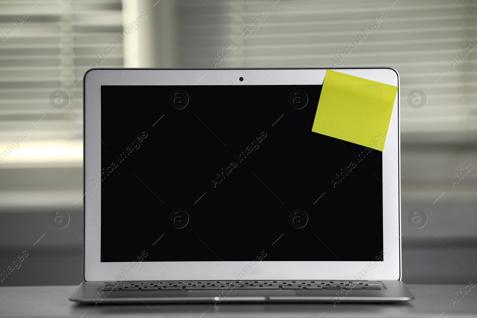 Photo of Laptop with blank sticky note on grey office desk. Space for text