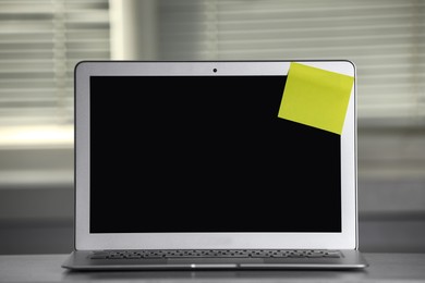 Photo of Laptop with blank sticky note on grey office desk. Space for text