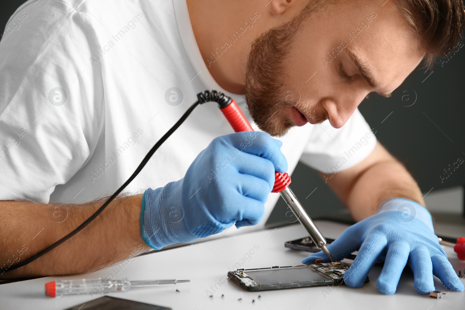 Photo of Young technician repairing mobile phone at table
