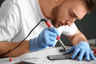 Young technician repairing mobile phone at table