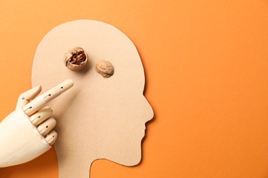 Photo of Amnesia problem. Paper cutout of human head, mannequin hand and broken walnut on orange background, top view. Space for text