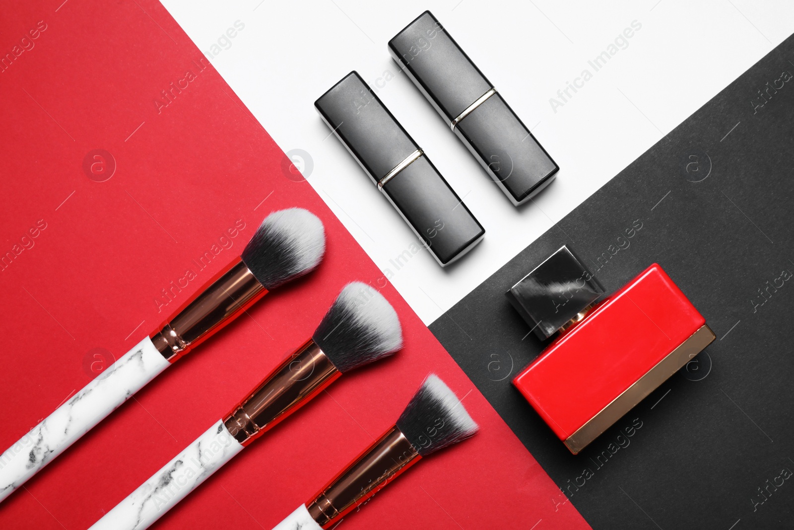 Photo of Makeup brushes, lipsticks and bottle of perfume on color background, flat lay