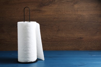 Photo of Holder with roll of white paper towels on blue wooden table. Space for text