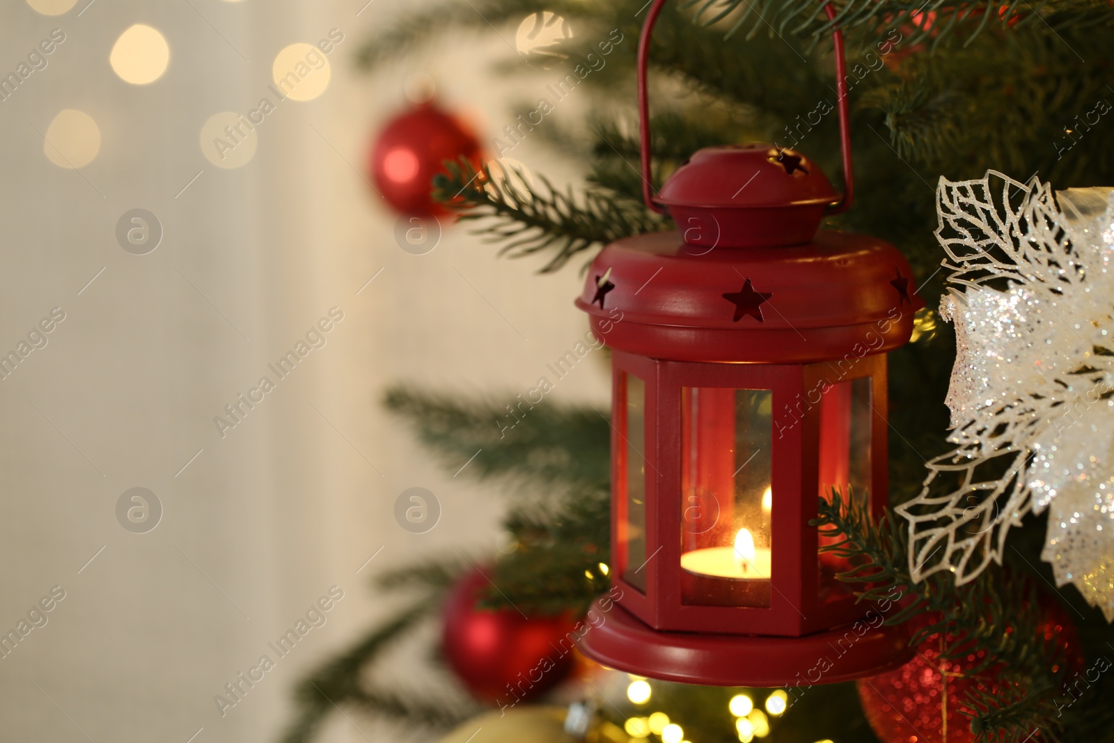 Photo of Christmas lantern with burning candle on fir tree indoors, closeup. Space for text