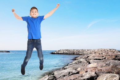 Image of Cute school boy jumping on beach near sea, space for text. Summer holidays
