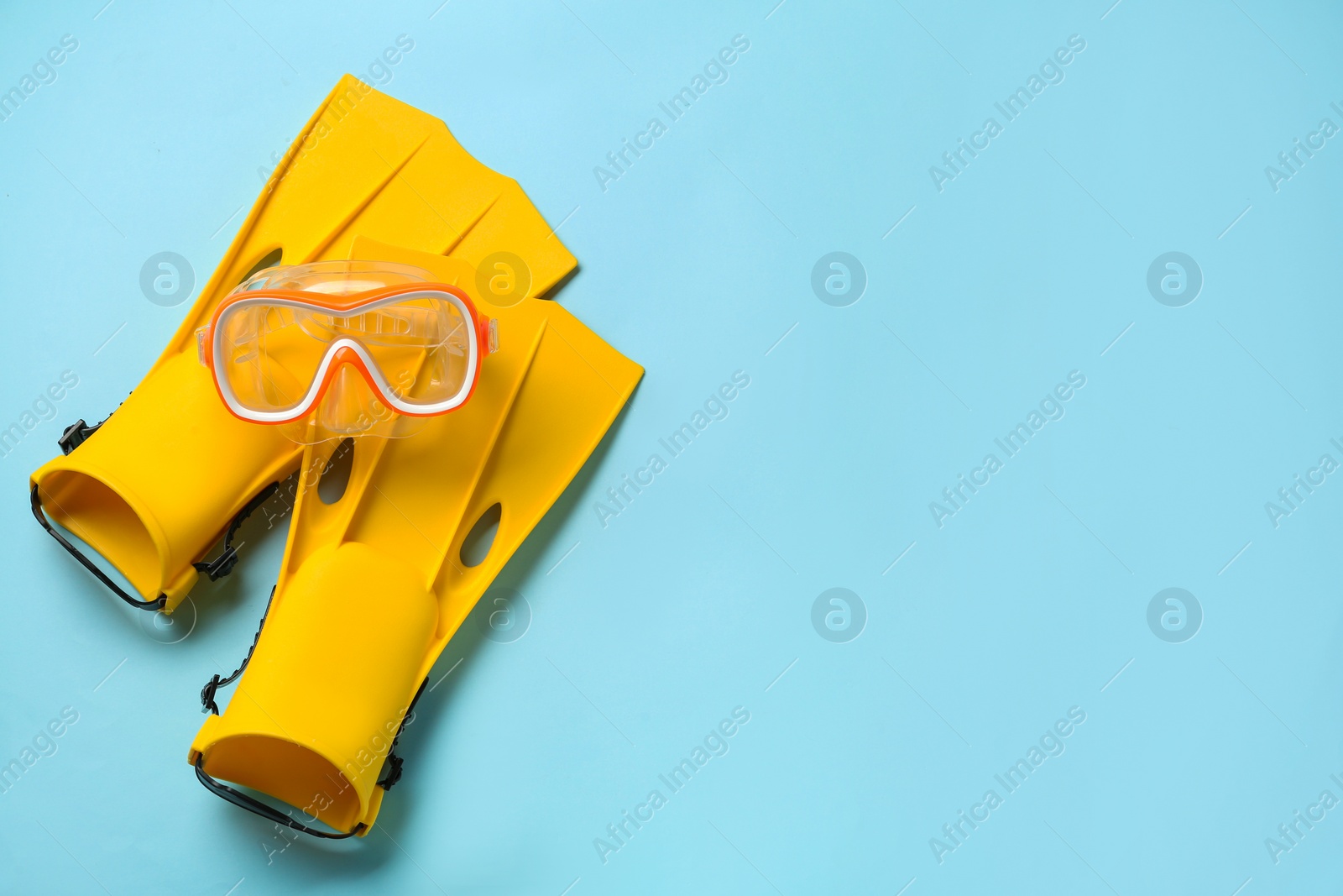 Photo of Pair of yellow flippers and mask on light blue background, flat lay. Space for text