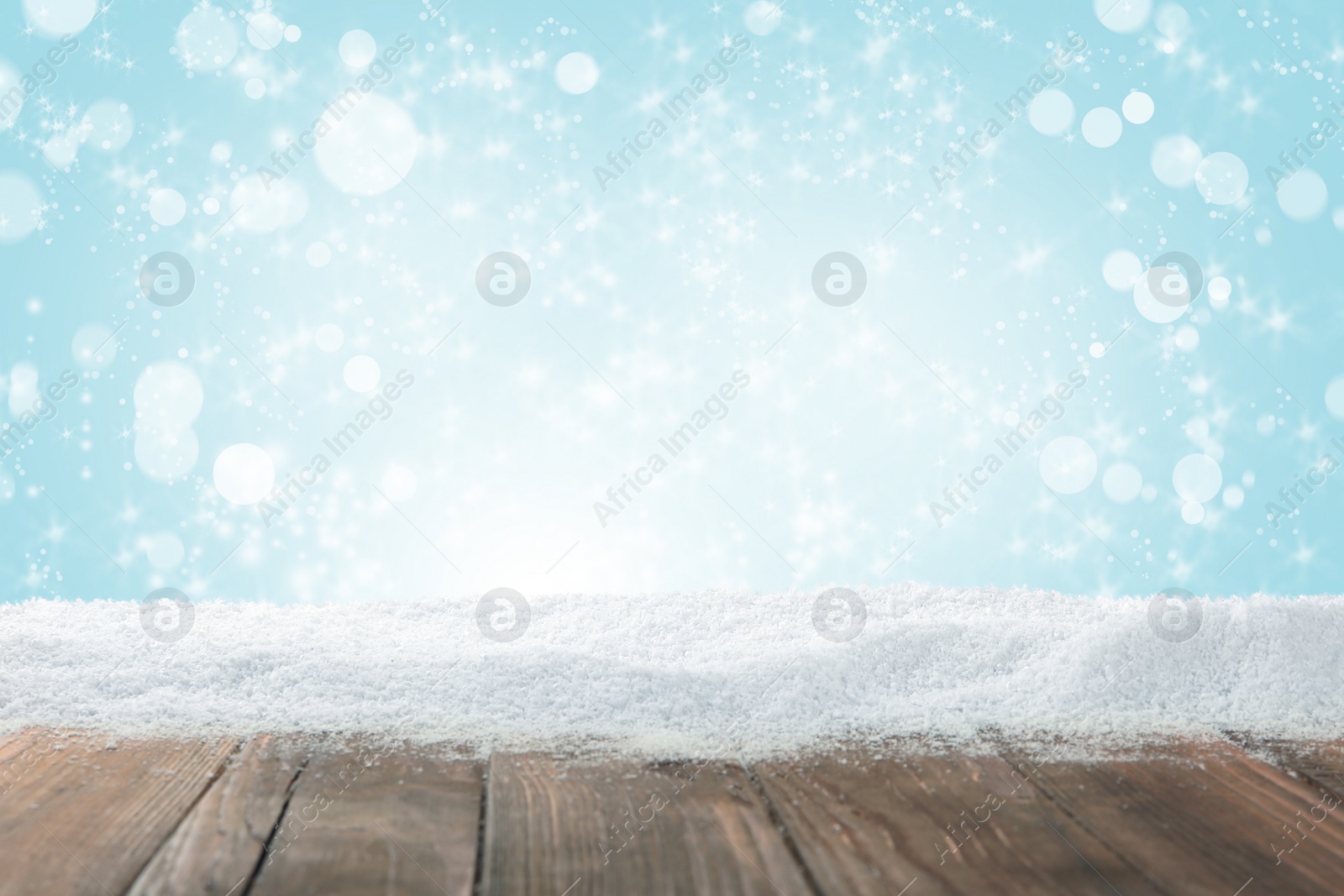 Image of Wooden surface with snow against light blue background, bokeh effect