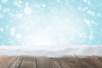 Image of Wooden surface with snow against light blue background, bokeh effect