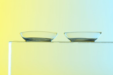 Photo of Pair of contact lenses on glass against light background, closeup
