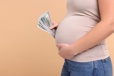 Photo of Surrogate mother. Pregnant woman with dollar banknotes on beige background, closeup. Space for text