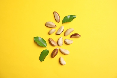 Flat lay composition with Brazil nuts and leaves on color background