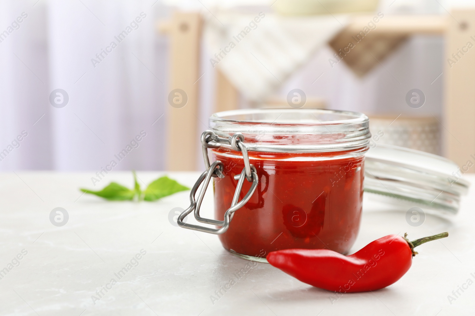 Photo of Jar with spicy chili sauce and fresh pepper on light table