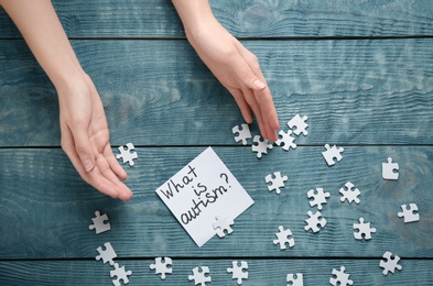 Woman, puzzle pieces and sticky note with phrase "What is autism?" on wooden background