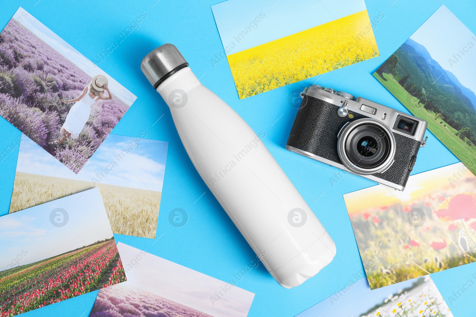 Photo of Stylish thermo bottle, camera and different photos on light blue background, flat lay