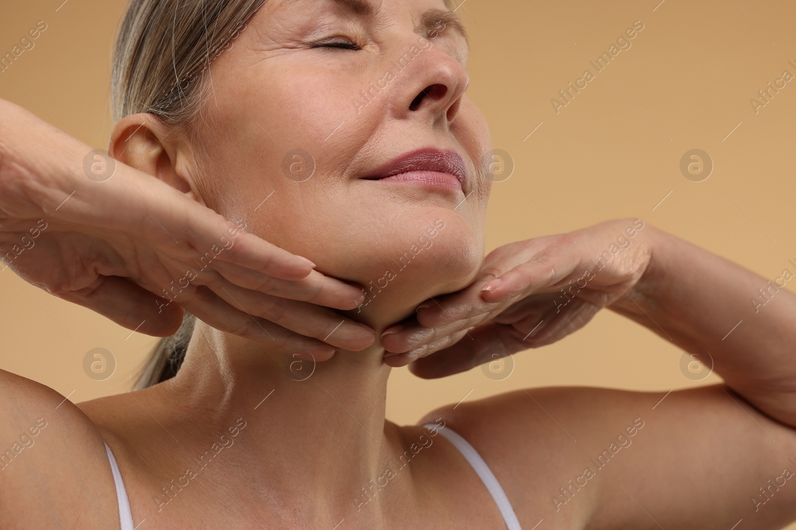 Photo of Beautiful woman touching her neck on beige background, low angle view