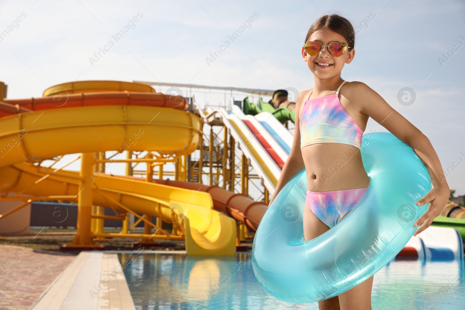 Photo of Cute little girl with inflatable ring near pool in water park, space for text