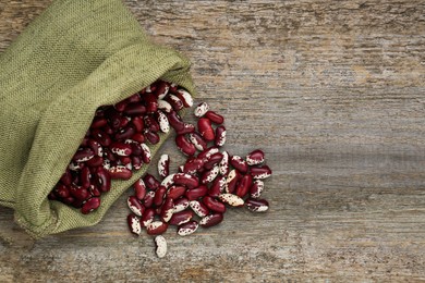 Photo of Overturned sack with dry kidney beans on old wooden table, flat lay. Space for text