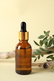 Photo of Bottle of cosmetic oil, branch and leaves on beige background, closeup