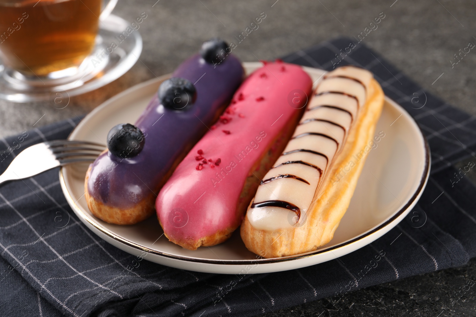 Photo of Different tasty glazed eclairs served on grey textured table, closeup