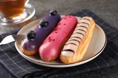 Different tasty glazed eclairs served on grey textured table, closeup