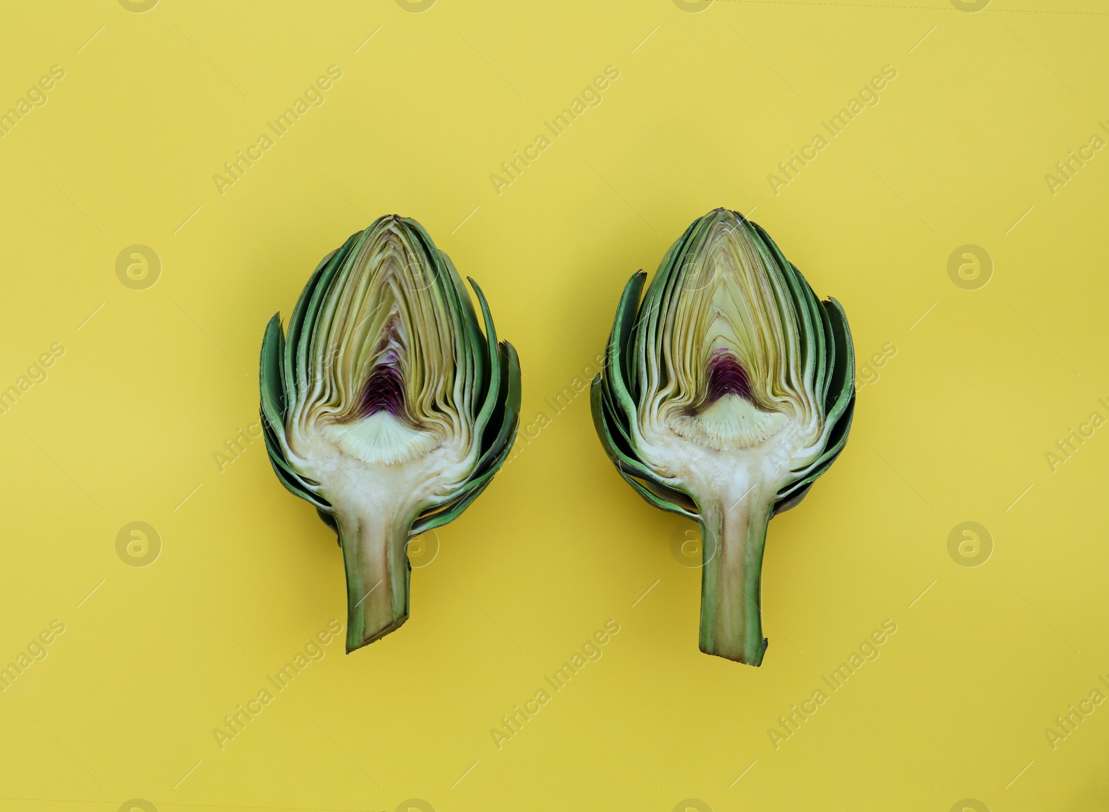 Photo of Cut fresh raw artichokes on yellow background, flat lay