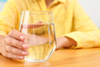 Woman holding glass of water at wooden table, closeup with space for text. Refreshing drink