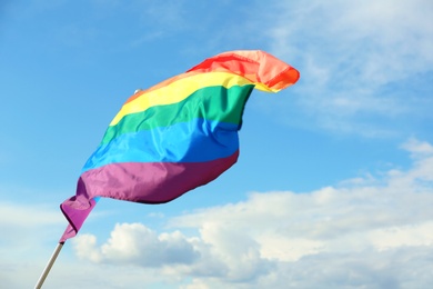 Photo of Bright rainbow gay flag fluttering against blue sky, space for text. LGBT community