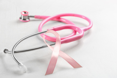 Photo of Pink ribbon and stethoscope on light grey stone background, closeup. Breast cancer concept