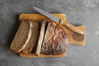 Photo of Board with bread and knife on grey background, top view