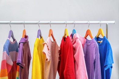 Photo of Colorful clothes hanging on wardrobe rack against light background