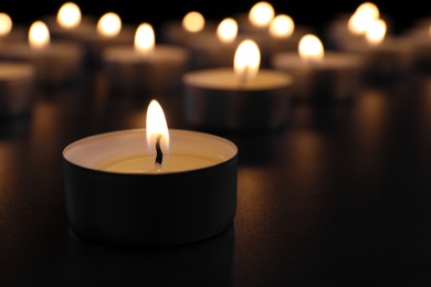 Photo of Burning candle on table in darkness, closeup with space for text. Funeral symbol