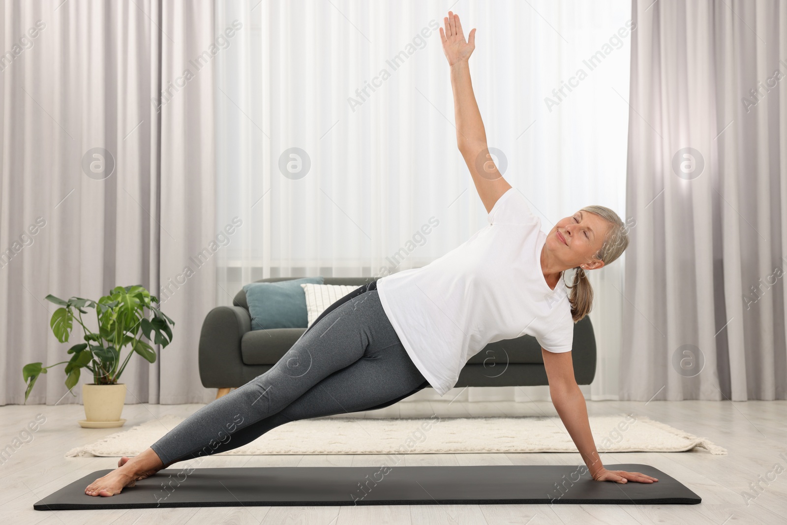 Photo of Happy senior woman practicing yoga on mat at home