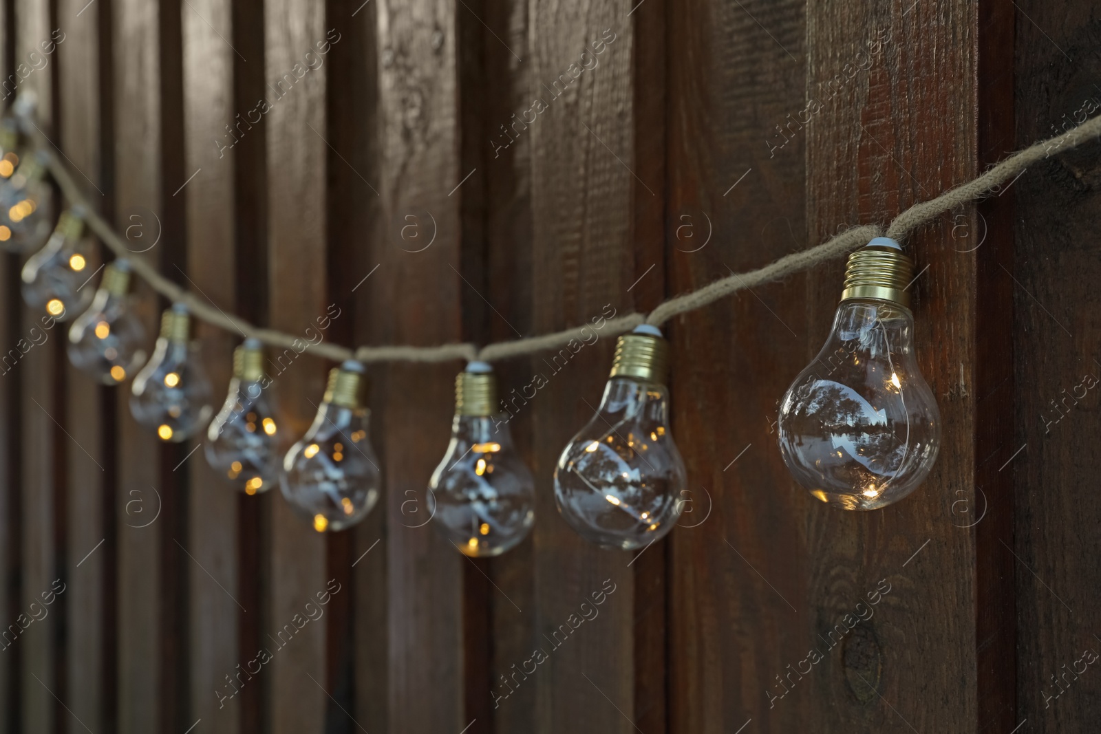 Photo of Garland of lamp bulbs hanging on wooden wall. String lights