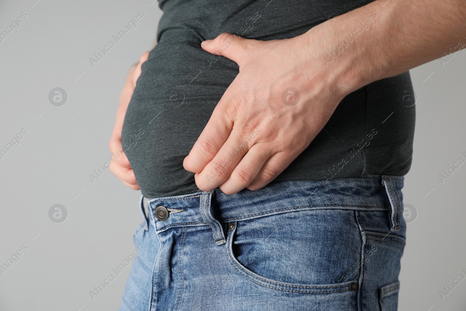 Photo of Overweight man in tight tshirt and jeans on light grey background, closeup