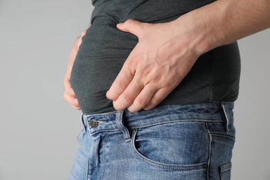 Photo of Overweight man in tight tshirt and jeans on light grey background, closeup