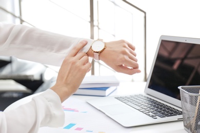 Young businesswoman checking time on her wristwatch at workplace. Time management