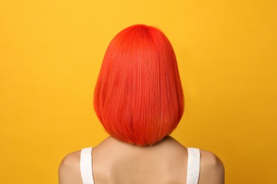 Photo of Young woman with bright dyed hair on orange background, back view