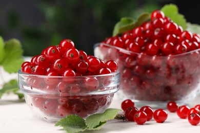 Many ripe red currants and leaves on white wooden table, closeup