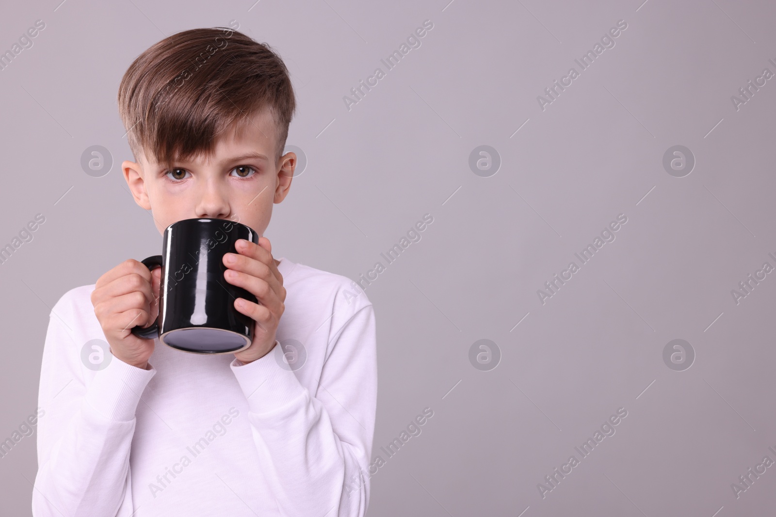 Photo of Cute boy drinking beverage from black ceramic mug on light grey background, space for text