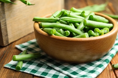 Photo of Fresh green beans in bowl on wooden table, closeup