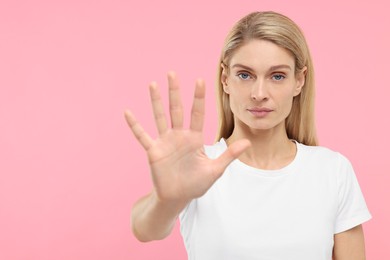 Photo of Woman showing stop gesture on pink background. Space for text
