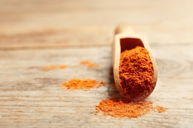 Photo of Scoop with powdered red pepper on wooden table. Space for text