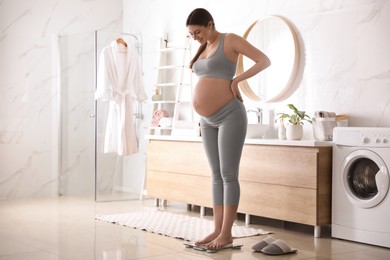 Photo of Pregnant woman standing on scales in bathroom